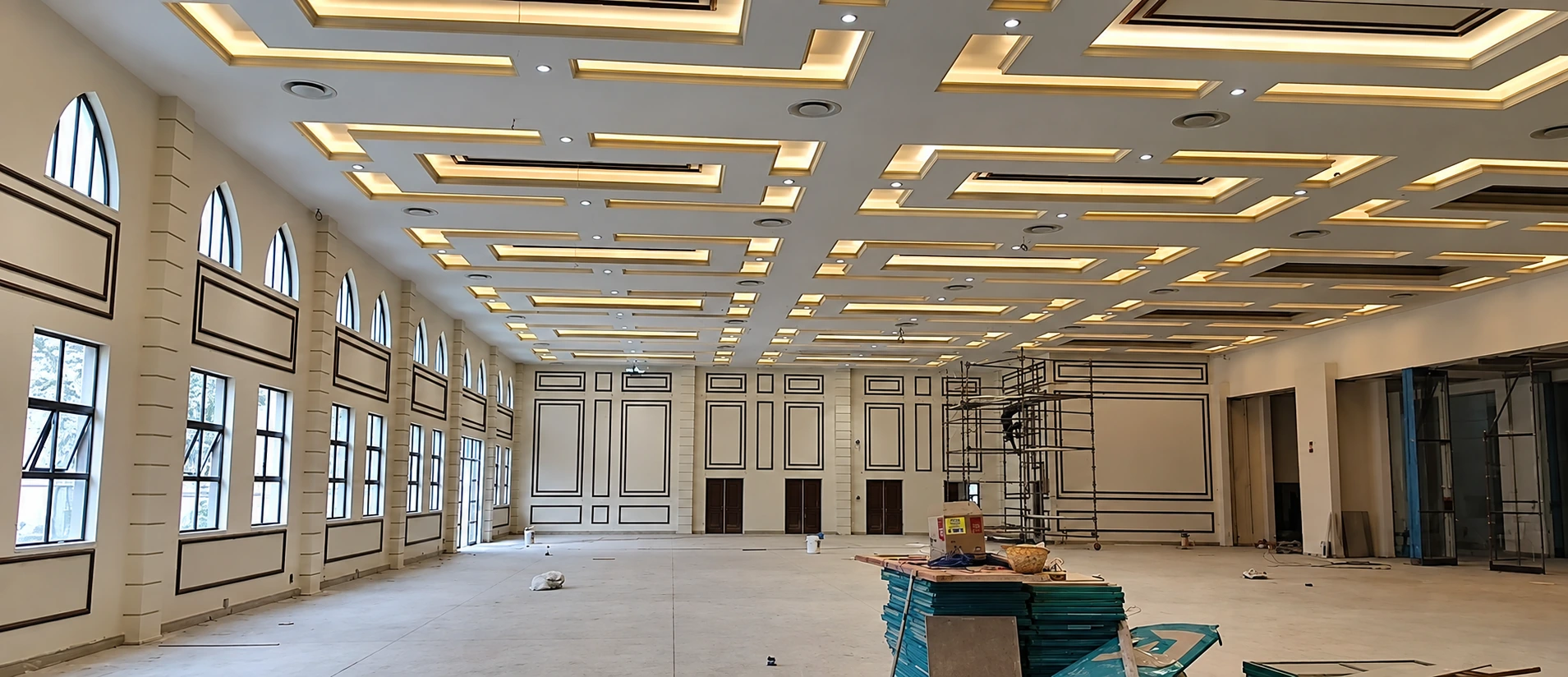 Large hall with repeated decorative ceiling geometry and warm lighting, with installation materials on site